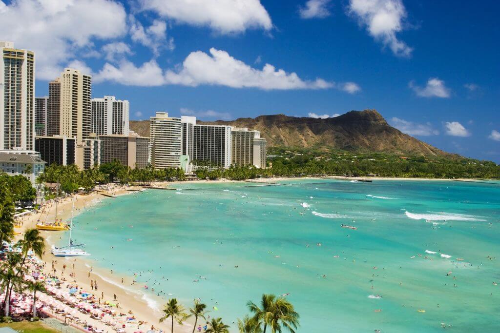 Waikiki beach is one of the best Oahu beaches for kids recommended by top Hawaii blog Hawaii Travel with Kids. Image of Waikiki bay with hotels and Diamond Head in the background.