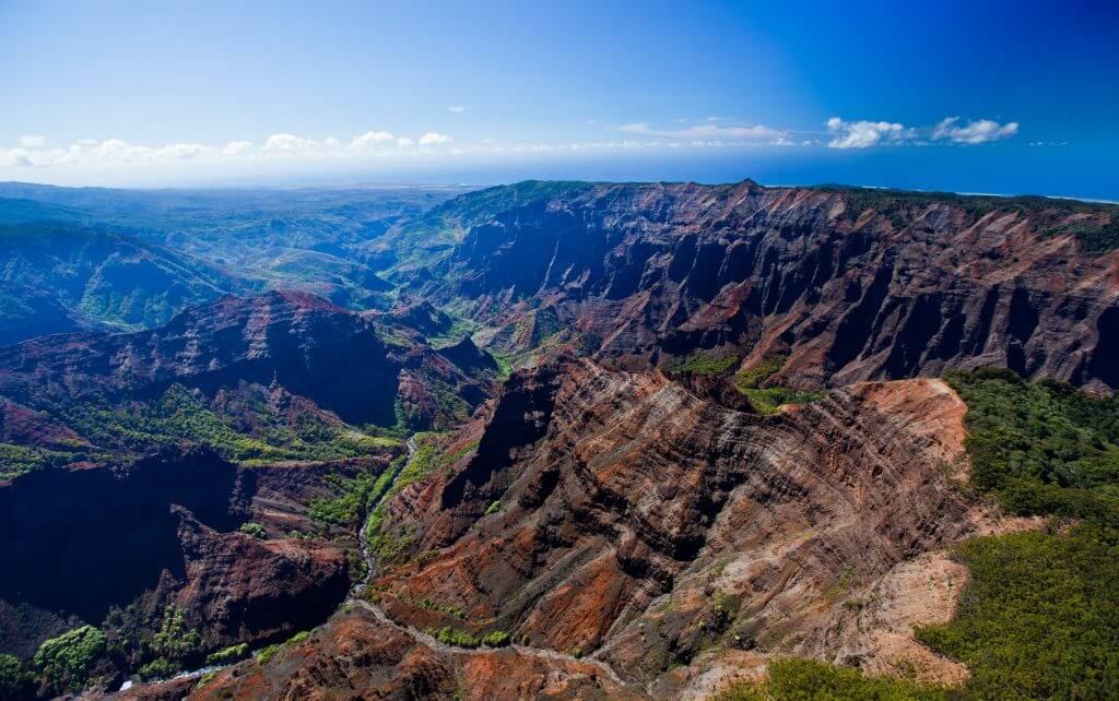 Waimea Canyon is one of the top Kauai attractions for families. Image of a canyon with blue sky and clouds.