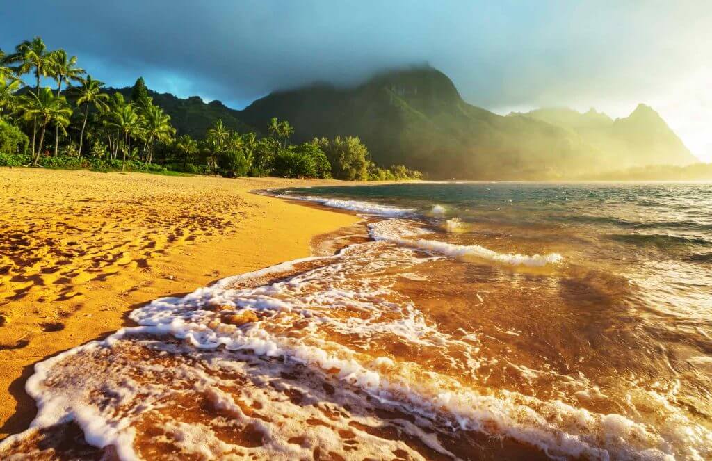 Tunnels Beach is one of the best places to snorkel on Kauai. Image of Tunnels Beach during golden hour with mountains in the background.