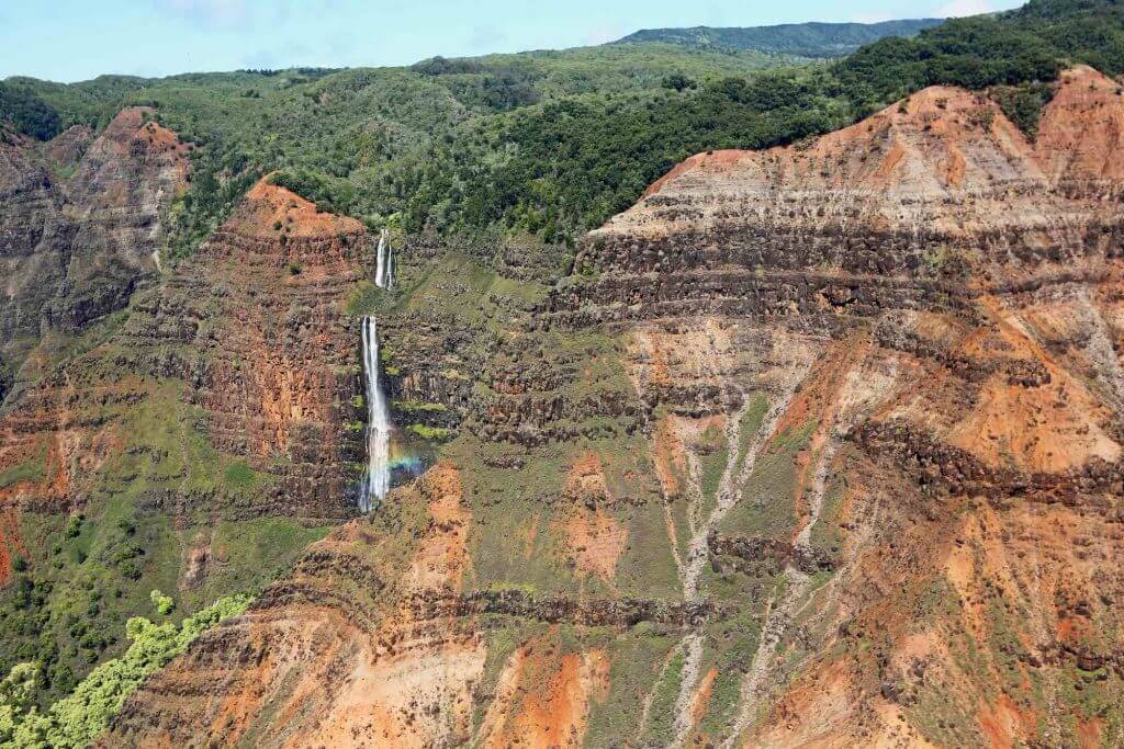 You'll definitely see Waimea Canyon on your Kauai helicopter ride. Image of a waterfall in Waimea Canyon, a top Kauai attraction.