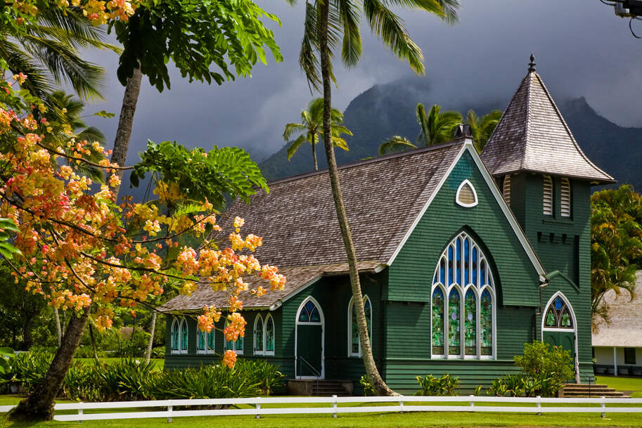 Waoli Huiia (aka Waioli Mission Church) the oldest church on the island of Kauai is one of the top Hanalei attractions. Image of a green church surrounded by palm trees.