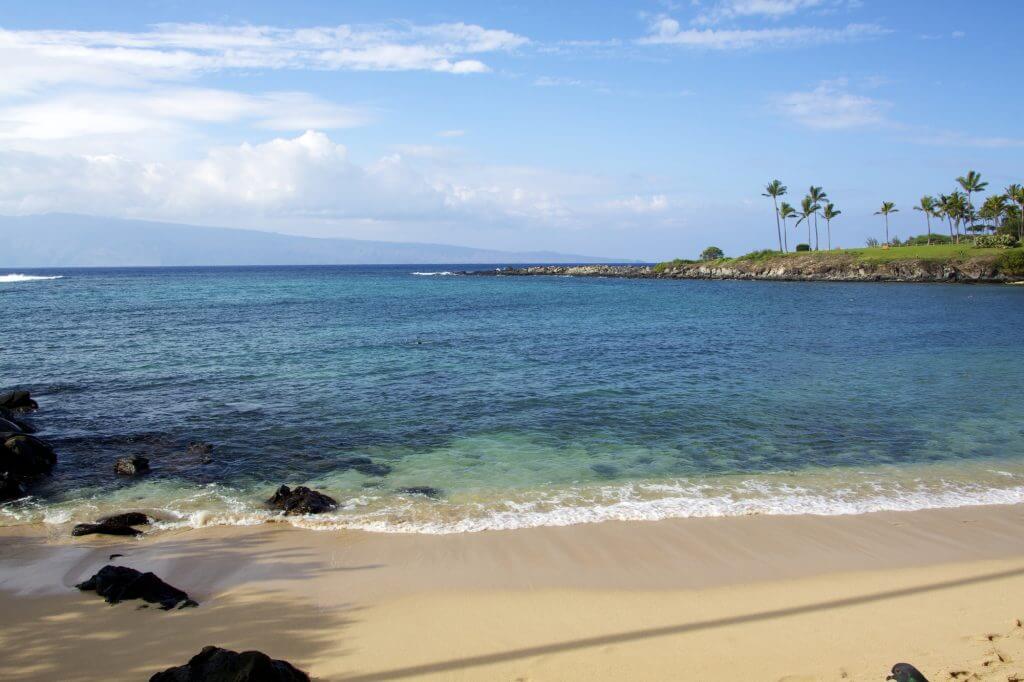 Kapalua Bay is one of the best Maui beaches for kids and is great for snorkeling. Image of a sandy beach and calm waves in Hawaii.