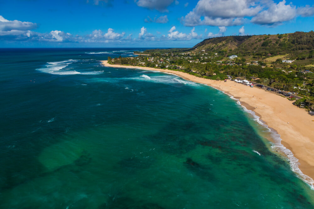 The Best 7 North Shore Oahu Beaches featured by top Hawaii blog, Hawaii Travel with Kids: Pupukea & Sunset Beach Parks in North Shore, Oahu. Image of a long golden sandy beach with blue/green ocean water.