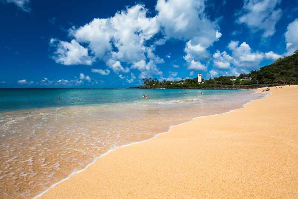 The Best 7 North Shore Oahu Beaches featured by top Hawaii blog, Hawaii Travel with Kids: Waimea Bay is a great snorkeling spot on Oahu. Image of a golden sandy beach with blue ocean water.