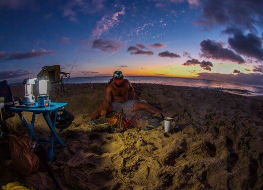 Guide to Camping in Hawaii featured by top Hawaii blog, Hawaii Travel with Kids. | You'll want to bring your own cooking equipment like this grill and cooler in the photo of a man camping in Hawaii