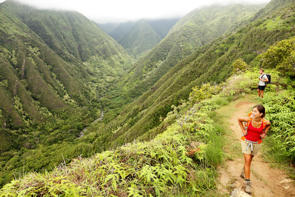 The Best Maui Hiking Trails featured by top Hawaii blog, Hawaii Travel with Kids: Hiking people on Hawaii, Waihee ridge trail, Maui, USA. Young woman and man hikers walking in beautiful lush Hawaiian forest nature landscape in mountains. Asian woman hiker in foreground.