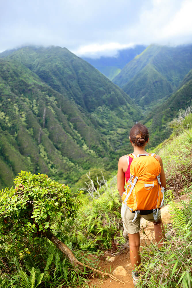 Hiking woman on Hawaii, Waihee ridge trail, Maui, USA. Young female hiker walking in beautiful lush Hawaiian forest nature landscape in mountains. Asian woman hiker wearing backpack looking at view.