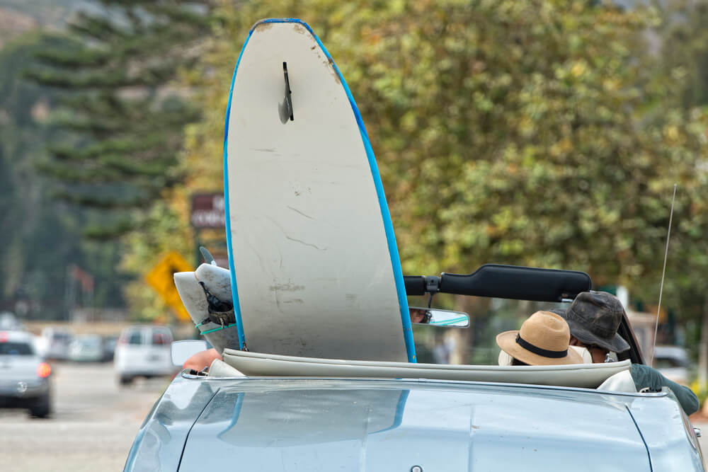 Find out how to rent a car in Hawaii by top Hawaii blog Hawaii Travel wth Kids. Image of a surfboard in a convertible.