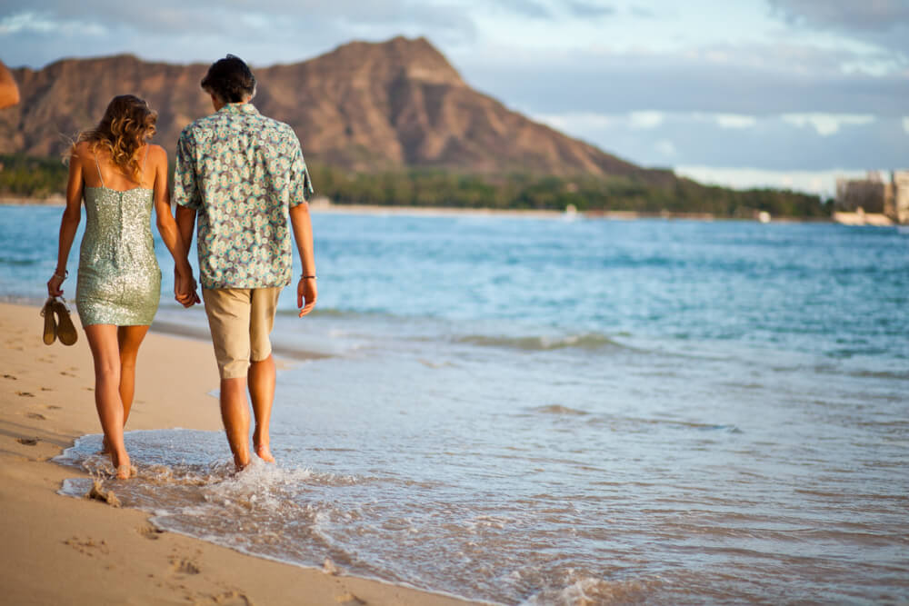 Visiting Hawaii in February with your Family, a travel guide featured by top Hawaii blog, Hawaii Travel with Kids: image of Couple walk along Waikiki with Leahi in back, Oahu