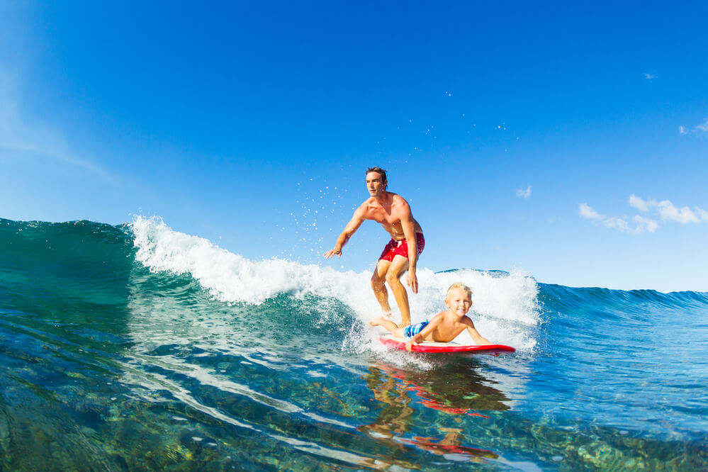 25 Amazing activities in Waikiki with kids featured by top Hawaii blog, Hawaii Travel with Kids: Father and Son Surfing Together Riding Blue Ocean Wave