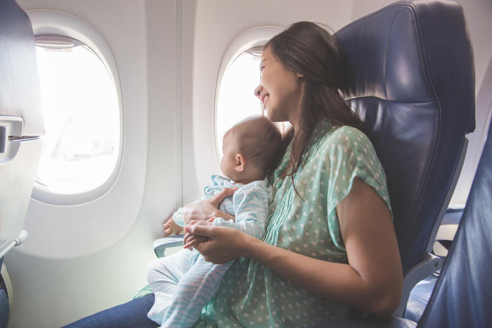 Find out my top tips for flying to Hawaii with a baby. Image of a mom holding a baby on her lap on an airplane.