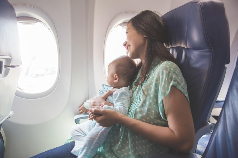 Best Travel Stroller for Hawaii featured by top Hawaii blog, Hawaii Travel with Kids: Happy mother and baby sitting together in airplane cabin near window