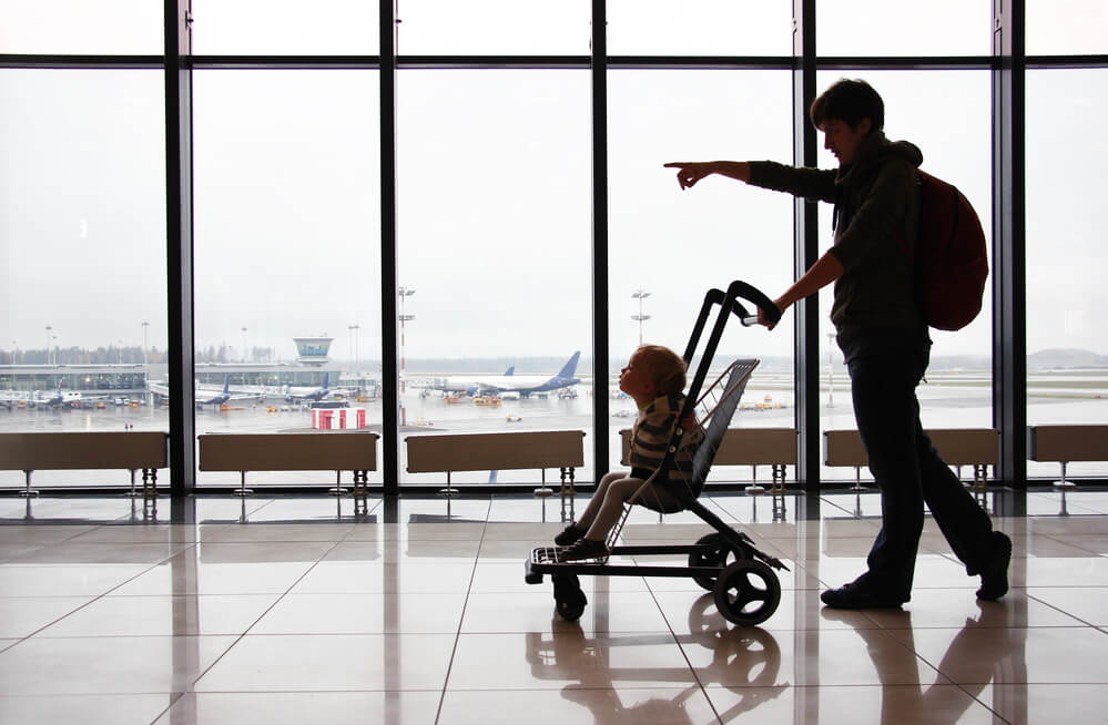 Get my tips for flying to Hawaii with a toddler. Image of a man pushing a stroller while pointing at an airport.