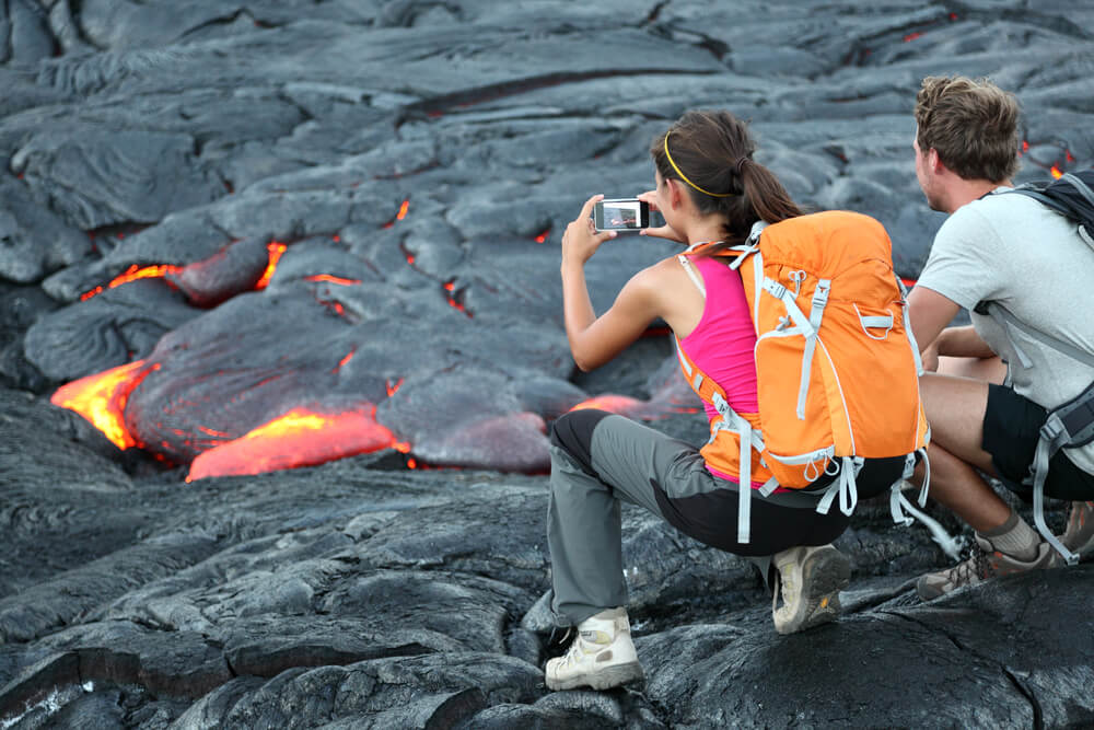 The Big Island grows 42 acres each year because of volcanic eruptions. Isn't that a crazy Hawaii fact? Image of tourists taking photo of flowing lava from Kilauea volcano around Hawaii volcanoes national park, USA.