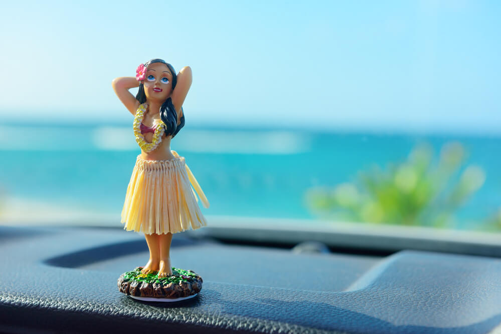 Find out how to save money on your Hawaii car rental by top Hawaii blog Hawaii Travel with Kids. Image of a dashboard hula doll in a car.