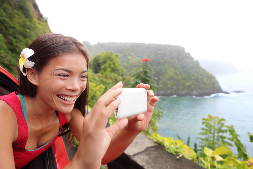 Renting a car in Hawaii is a smart idea. Image of a tourist on Hawaii taking photo with camera phone during car road trip on the famous Road to Hana