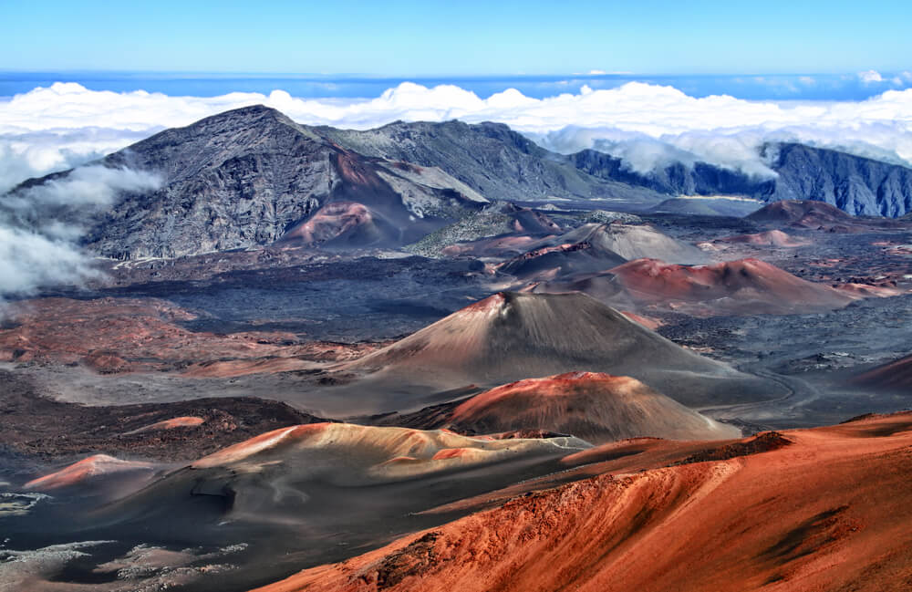 Haleakala Crater on Maui is one of the best Hawaii National Parks to check out. Image of the crater with clouds around it.