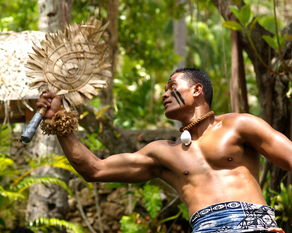 The Polynesian Cultural Center is one of the best Hawaii tourist destinations for families. Image of a Fijian performer wearing paint on his face.