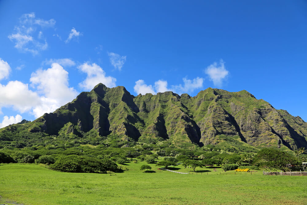 Kualoa Ranch on Oahu is a great stop when Honolulu sightseeing. Image of a green mountain with jagged cliffs.