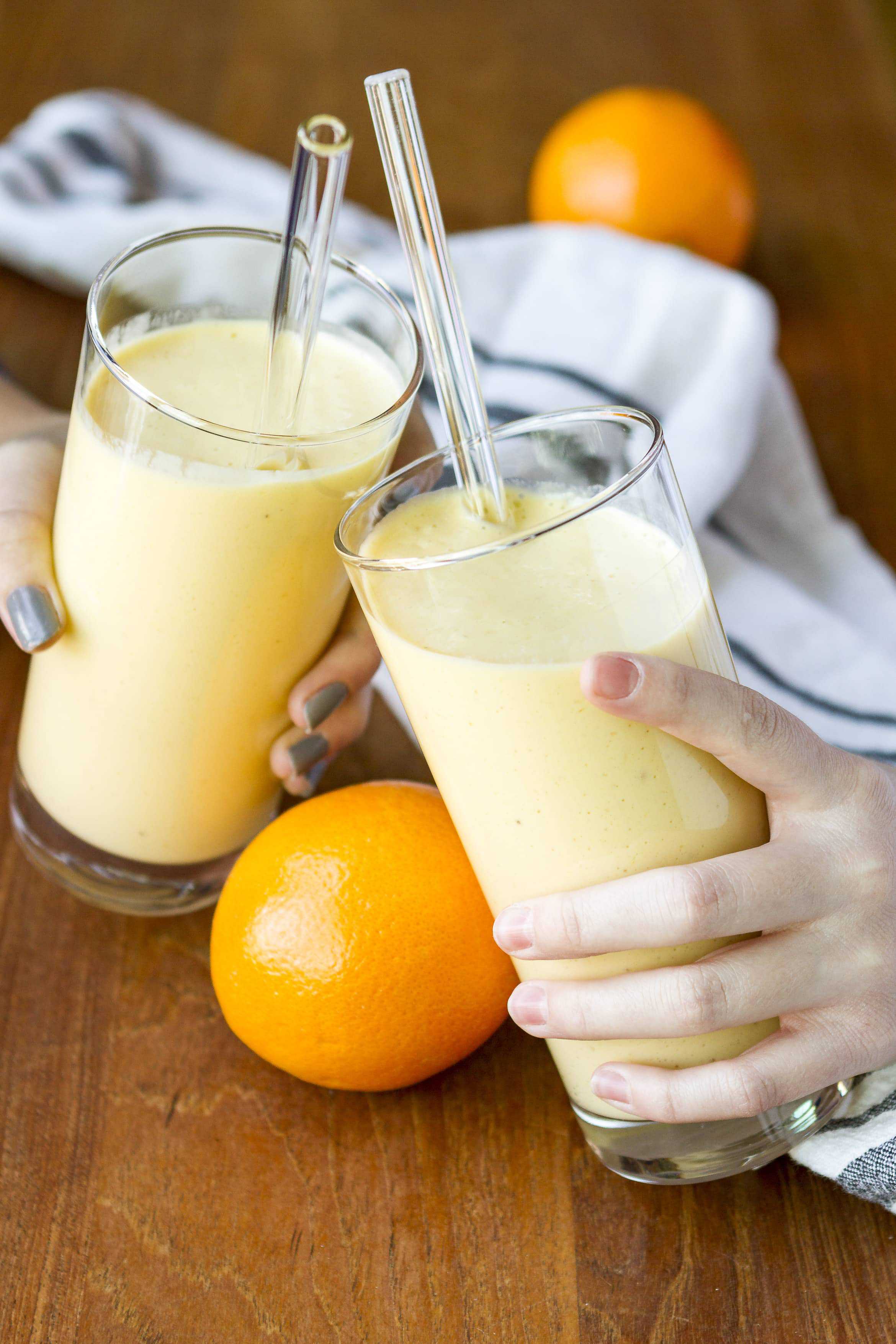 Hawaiian Tropical Smoothie Recipes to Make at Home featured by top Hawaii blog, Hawaii Travel with Kids: clinking glasses filled with orange mango healthy citrus smoothie