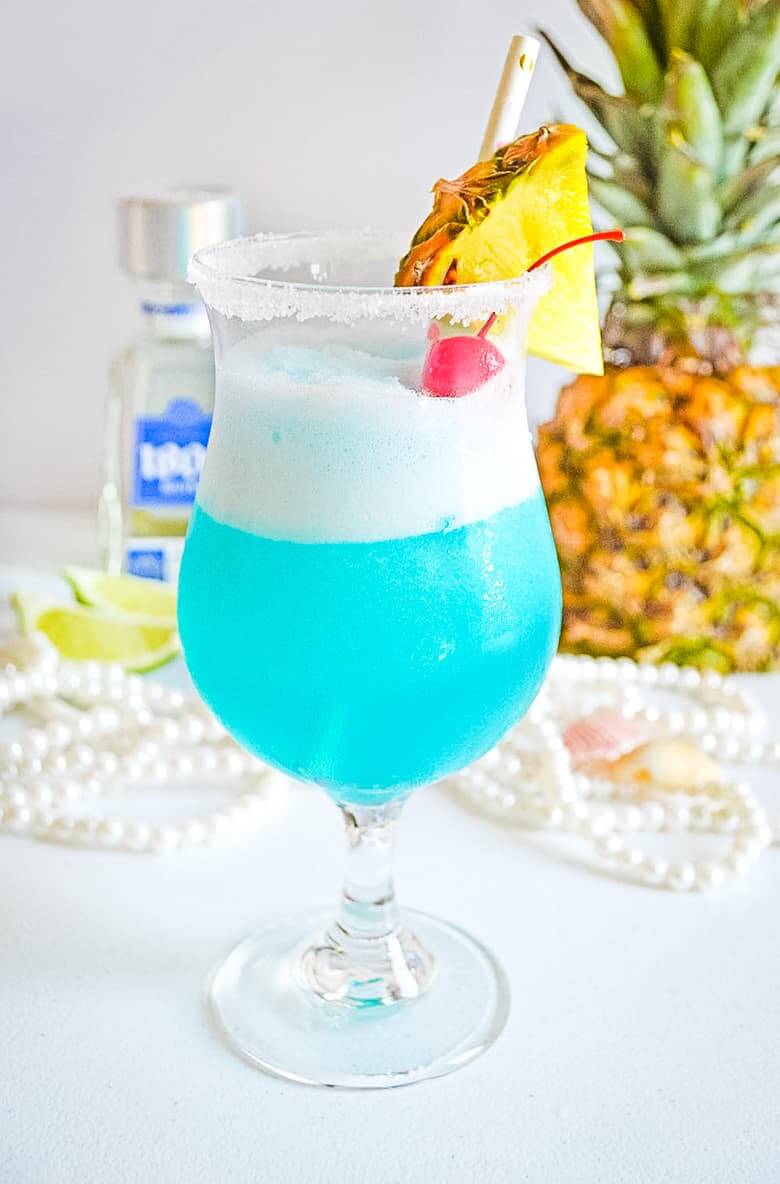 40 Hawaiian Cocktails To Try At Home featured by top Hawaii blog, Hawaii Travel with Kids: Frozen blue cocktail garnished with fresh pineapple and maraschino cherry