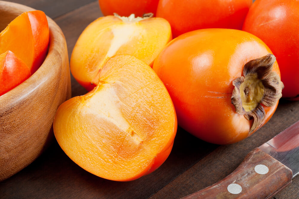 15 Hawaiian Fruits to Try featured by top Hawaii blog, Hawaii Travel with Kids: Persimmons on a wooden table