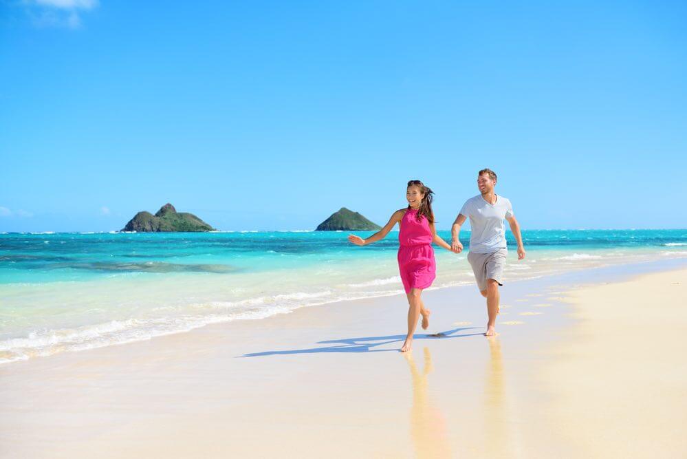 Beach happy couple on running having fun on Hawaii. Romantic couple joyful and full of happiness on travel vacation on Lanikai beach, Oahu, Hawaii, USA with Mokulua Islands. Asian woman, Caucasian man