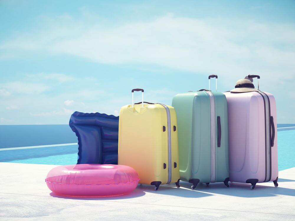 Learn more about travel insurance for Hawaii by top Hawaii blog Hawaii Travel with Kids. Image of colorful suitcase and white hat next to the swimming pool