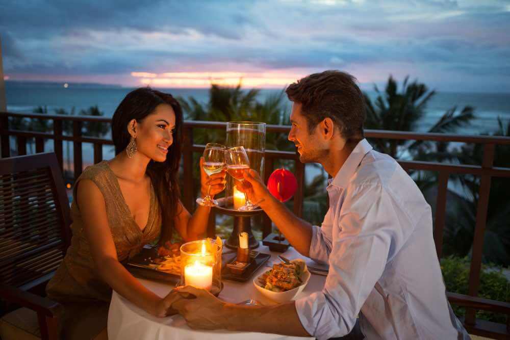 Top 15 Things to do on Your Hawaii Honeymoon featured by top Hawaii blog, Hawaii Travel with Kids: young couple enjoying a romantic dinner by candlelight, outdoor on Hawaii honeymoon