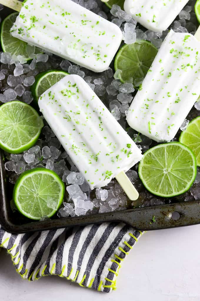 61 Delicious Coconut Dessert Recipes Perfect for Summer featured by top Hawaii blog, Hawaii Travel with Kids: 4 coconut lime popsicles on a baking tray with ice and lime slices. 