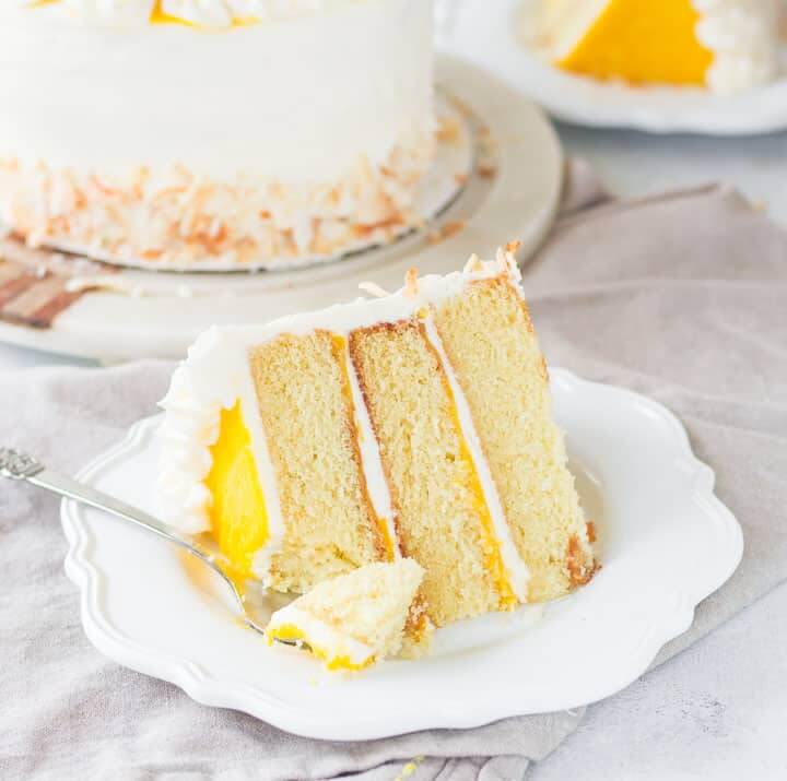 61 Delicious Coconut Dessert Recipes Perfect for Summer featured by top Hawaii blog, Hawaii Travel with Kids: slice of mango coconut cake sitting on a plate with a fork taking a bite out of it