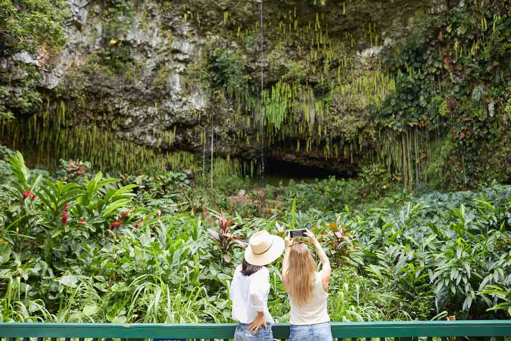 Fern Grotto is a popular Kauai attraction and one of the top things to do in Lihue Kauai. Image of two women taking a photo of Fern Grotto.