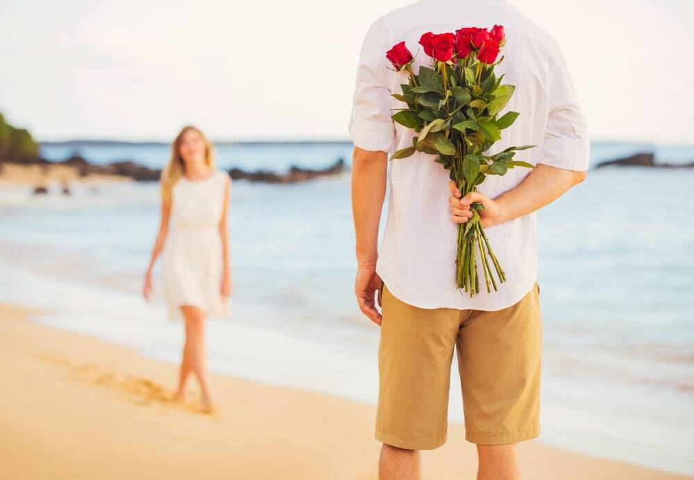 Top 10 Romantic Hawaii Beach Proposal Ideas + Locations featured by top Hawaii blog, Hawaii Travel with Kids: Young Couple in Love, Man holding surprise bouquet of roses for beautiful young woman, Romantic Date