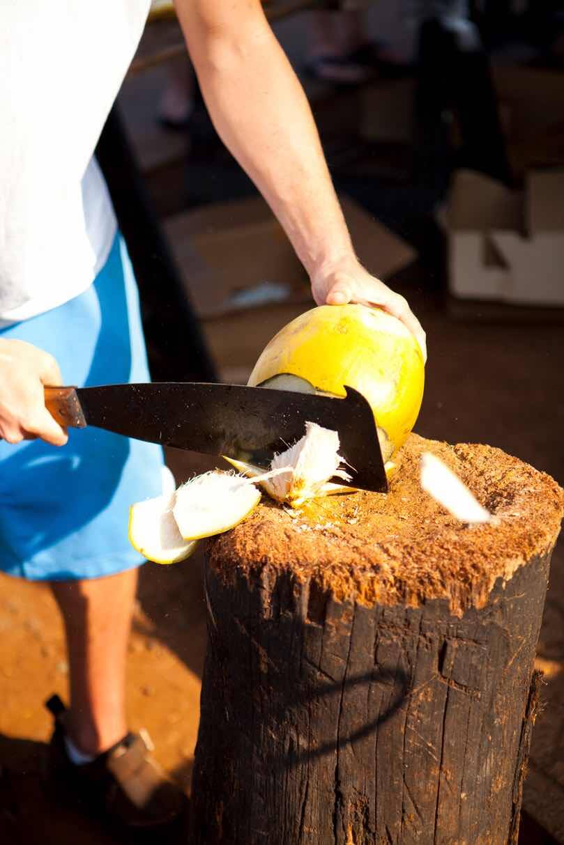 7 Best Maui Farmers Markets Worth Checking Out featured by top Hawaii travel blog, Hawaii Travel with Kids: Image of a man chopping a coconut with a machete.