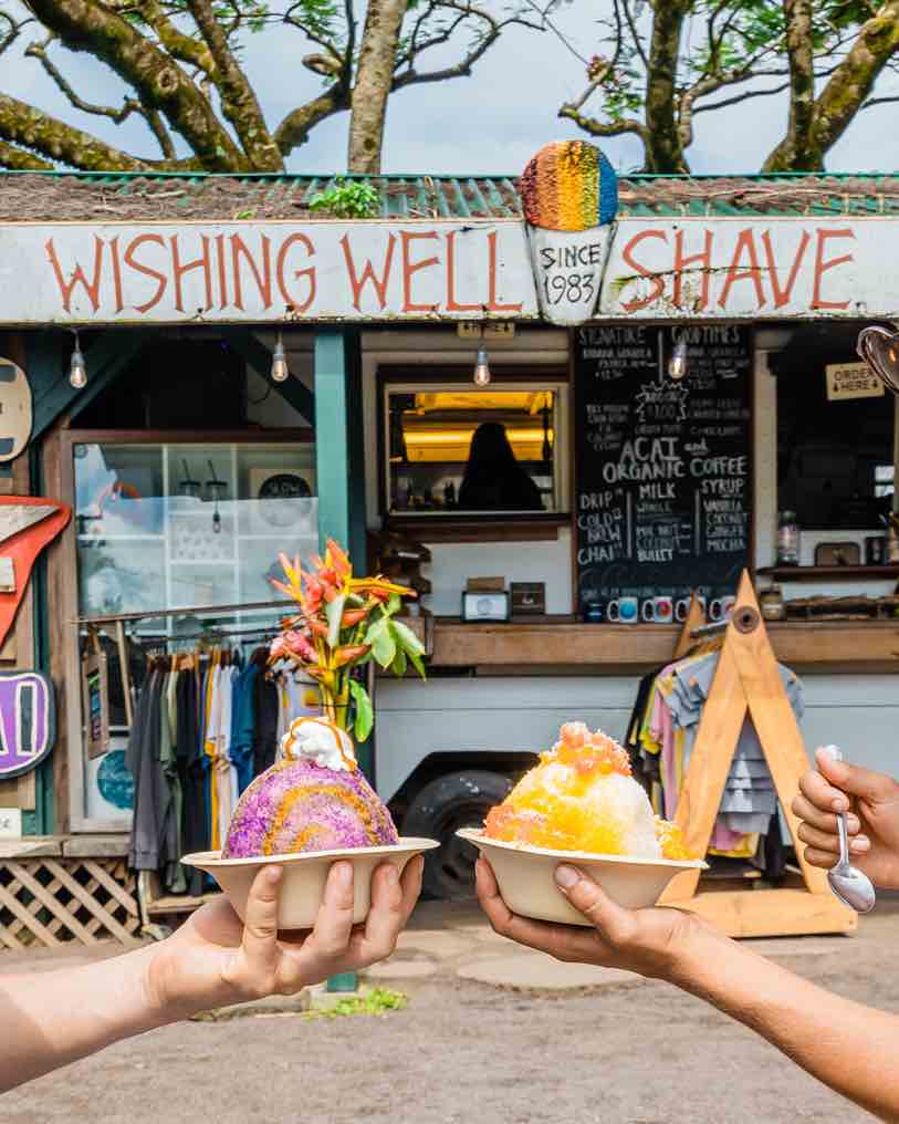 Wishing Well Shave Ice is one of my favorite things to do in Hanalei Kauai! Image of the Wishing Well Shave Ice sign with people holding bowls of colorful shave ice in front of the truck.