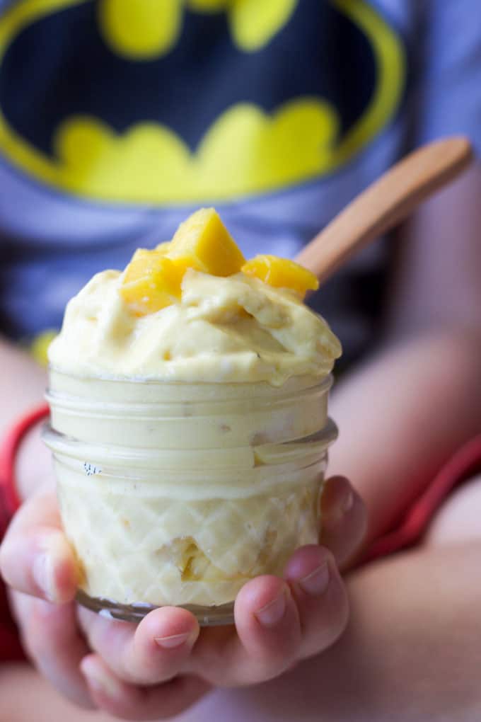 Best Mango dessert recipes by top Hawaii blog Hawaii Travel with Kids: Child holding tub of homemade mango frozen yogurt topped with mango pieces