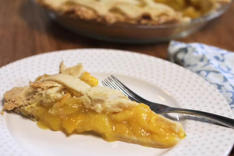 Best Mango dessert recipes by top Hawaii blog Hawaii Travel with Kids: image of a slice of mango lime pie and a fork on white plate with gold dots, with a pie in a pie pan in the background, and blue and white napkin beside the plate