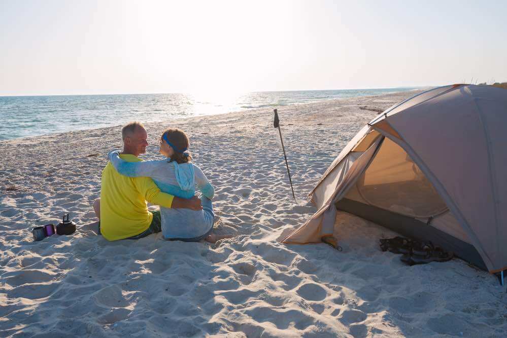 Camping in Maui: Romantic couple is relaxing near a tent on the beach, hugging and looking at each other. Happy people in nature. Back Light.