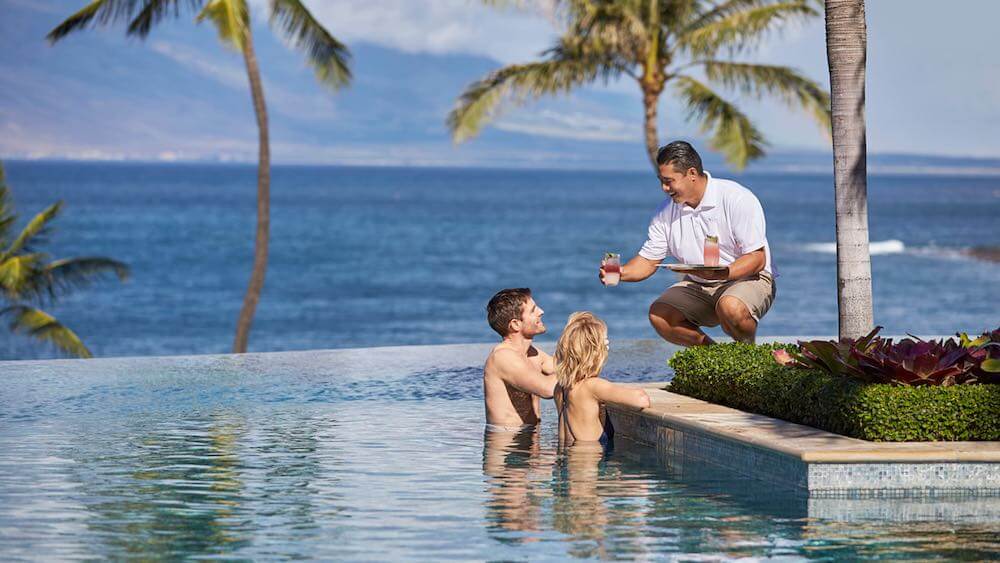 The Four Seasons Maui is just one of the top Maui Luxury Hotels worth checking out. Image of a couple in an infinity pool in Maui