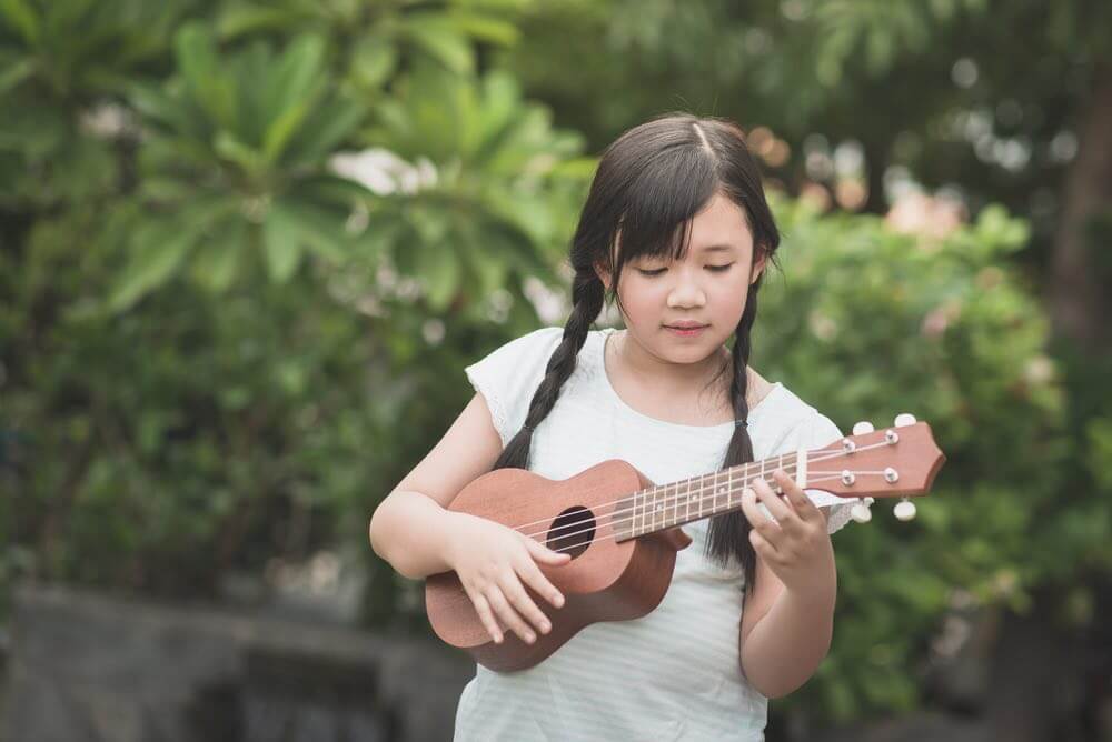 Even though it's a Portuguese instrument, many people associated ukuleles with Hawaii. Image of a girl playing a kids ukulele