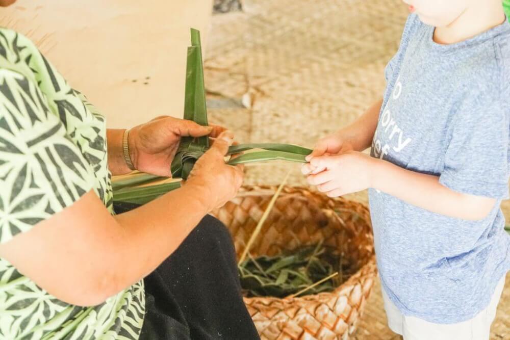 The Polynesian Cultural Center is the best rated luau in Oahu. Image of a boy learning how to weave lauhala at the Polynesian Cultural Center in Laie Oahu.