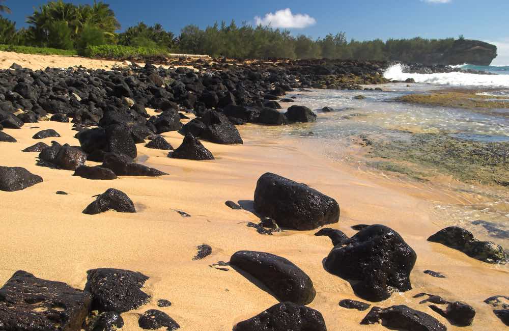 Shipwreck Beach is a top sunset Kauai spot. Image of Shipwreck Beach with black volcanic boulders, Kauai, Hawaii