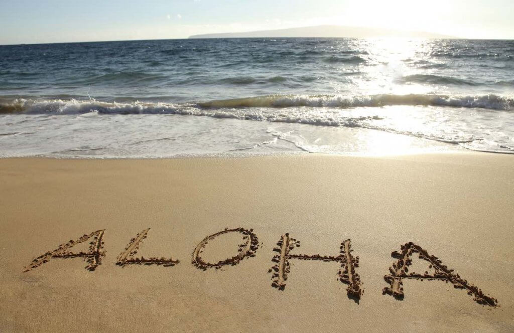 It helps to learn a few Hawaiian words before traveling to Hawaii for the first time. Image of the word Aloha written in the sand.