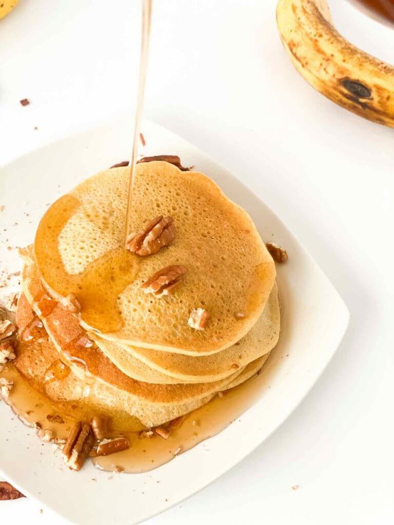You can serve these gluten free dairy free banana pancakes with pure maple syrup and nuts. Image of someone pouring maple syrup on banana pancakes.