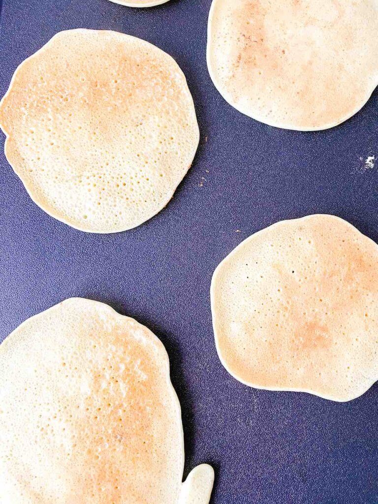 You'll know this pancake recipe with gluten free flour is done when they turn golden brown. Image of slightly golden Hawaiian banana pancakes on a griddle.