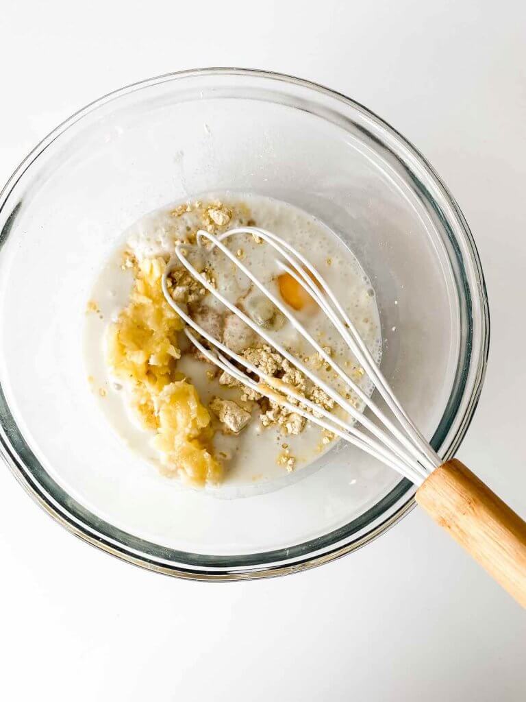 Whisk all the gluten free banana pancakes recipe ingredients together in a bowl. Image of a Pyrex bowl with whisk and all the ingredients.