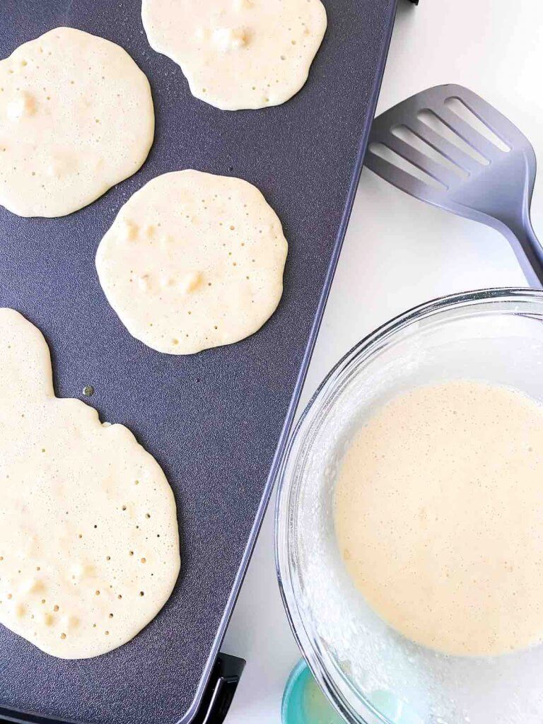 You can make this easy banana pancake recipe on the griddle or a pan on the stove. Image of pancakes cooking on a griddle.