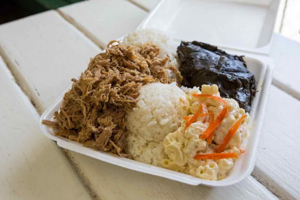 One of the best things to eat in Hawaii is a Hawaiian plate lunch. Image of a takeout box with kalua pork, lau lau, macaroni salad, and rice.