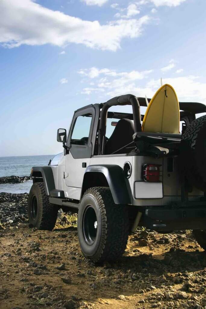 One of my top Maui tips is to rent a car. Image of SUV parked at beach with surfboard in Maui, Hawaii.