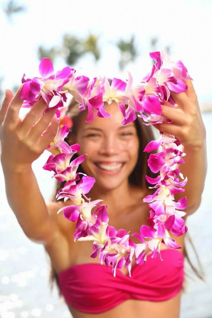 Do you still get a lei at the airport in Hawaii? Only if you arrange for it. Image of Hawaii woman showing flower lei garland of pink orchids. Beautiful smiling mixed race woman in bikini on beach giving a welcoming Lei on the hawaiian island Big Island.